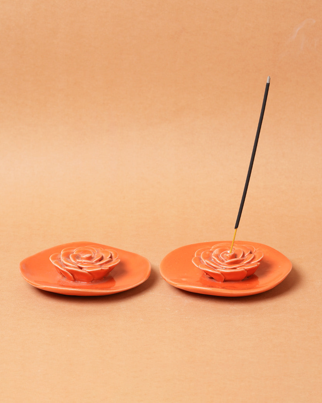 Two orange incense holders with incense sticks on a beige background