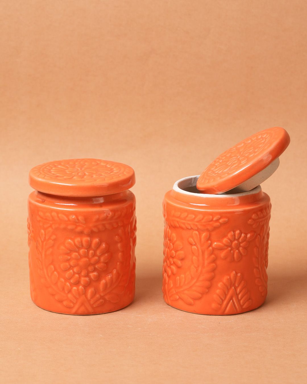 Two orange ceramic jars with embossed designs on a beige background