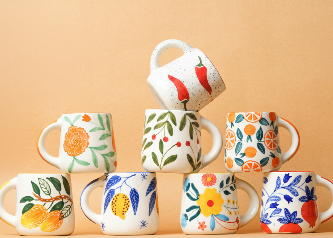 Set of colorful ceramic mugs with floral and fruit designs on a beige background