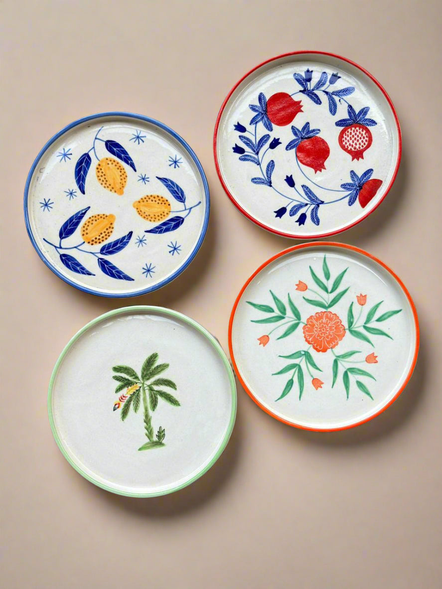 Four ceramic plates with floral and botanical designs on a textured surface
