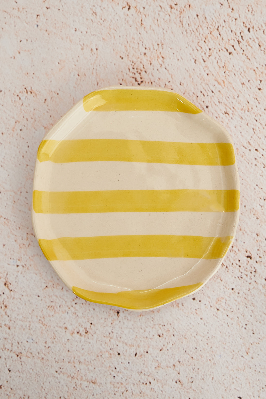 Yellow and white striped ceramic plate on a textured beige surface