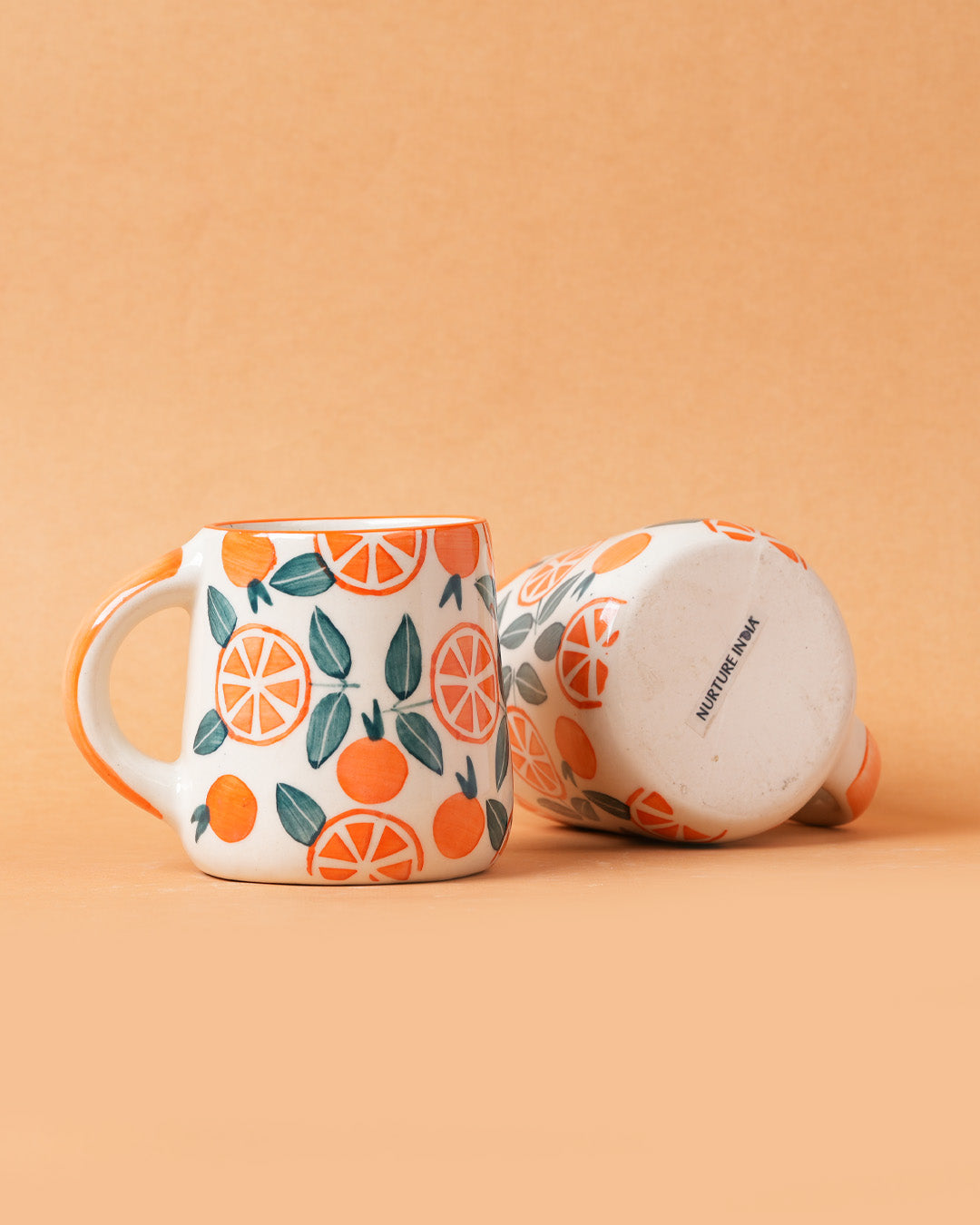 Ceramic mug with orange and leaf pattern on a peach background
