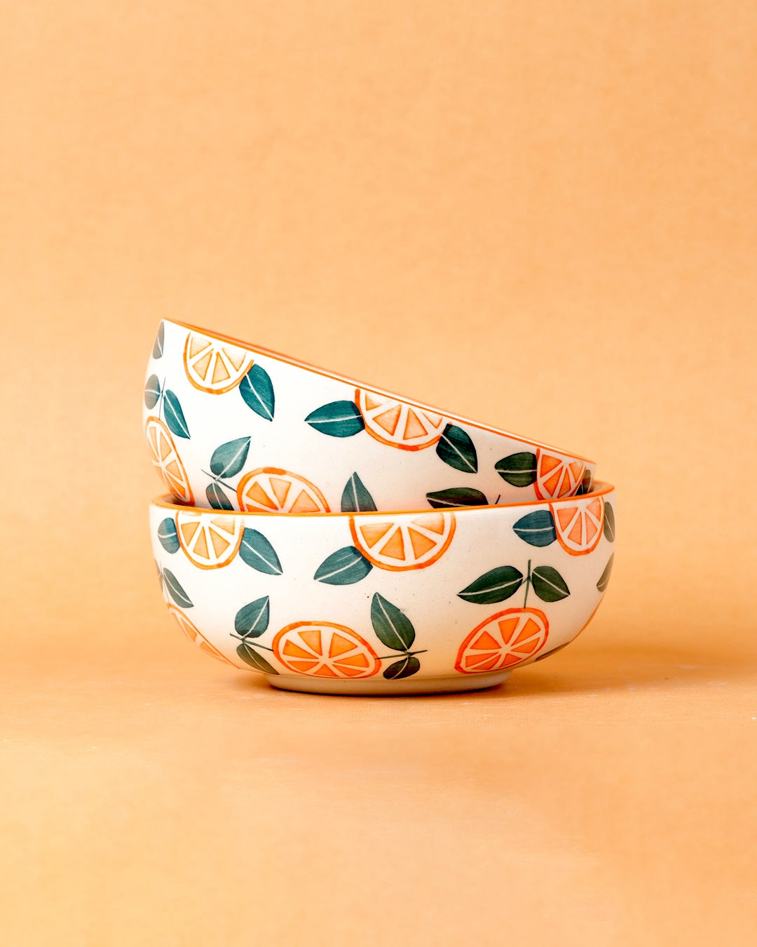Two ceramic bowls with orange and leaf pattern on a peach background