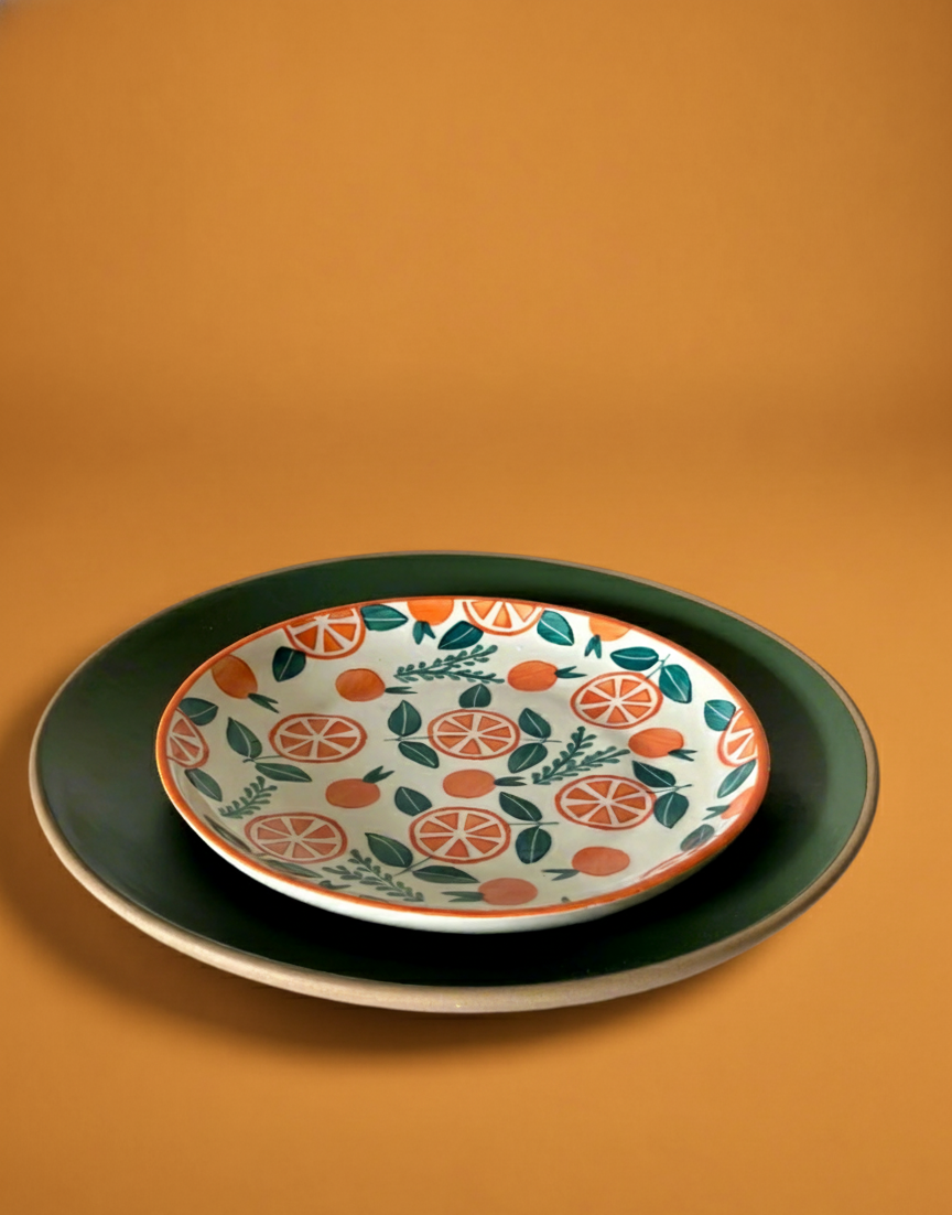 Decorative plate with orange and green pattern on a matching platter against an orange background