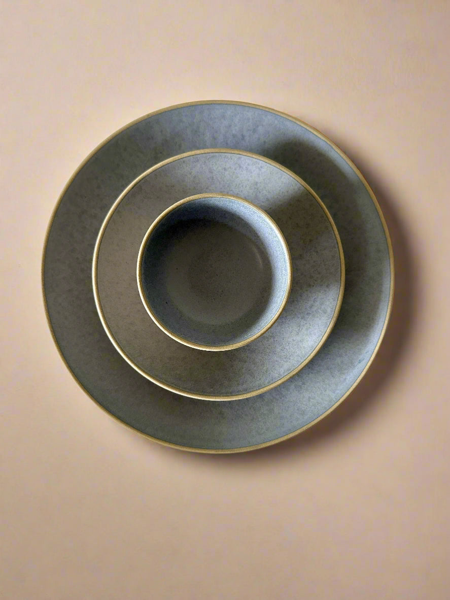 Set of three gray ceramic plates with gold rims on a textured white surface