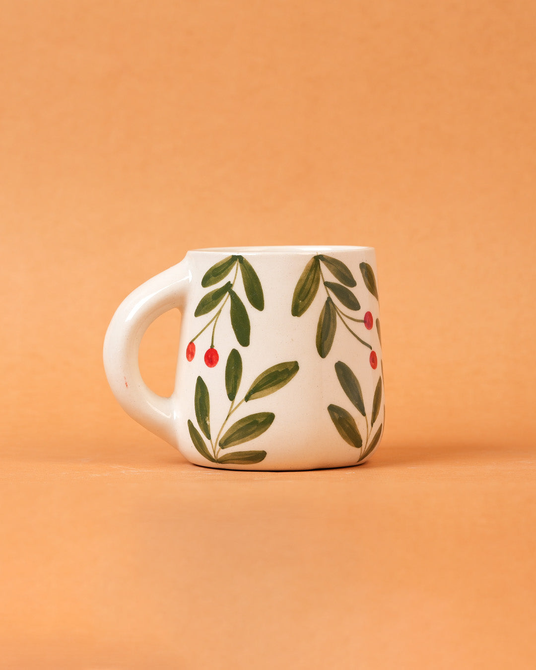 White mug with green leaf and red berry design on an orange background