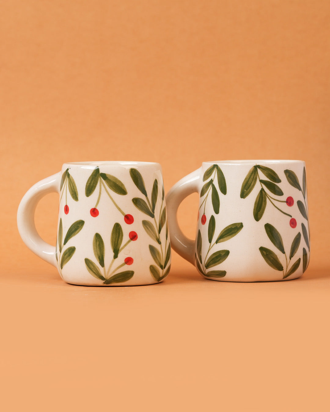 Two ceramic mugs with leaf and berry design on a peach background