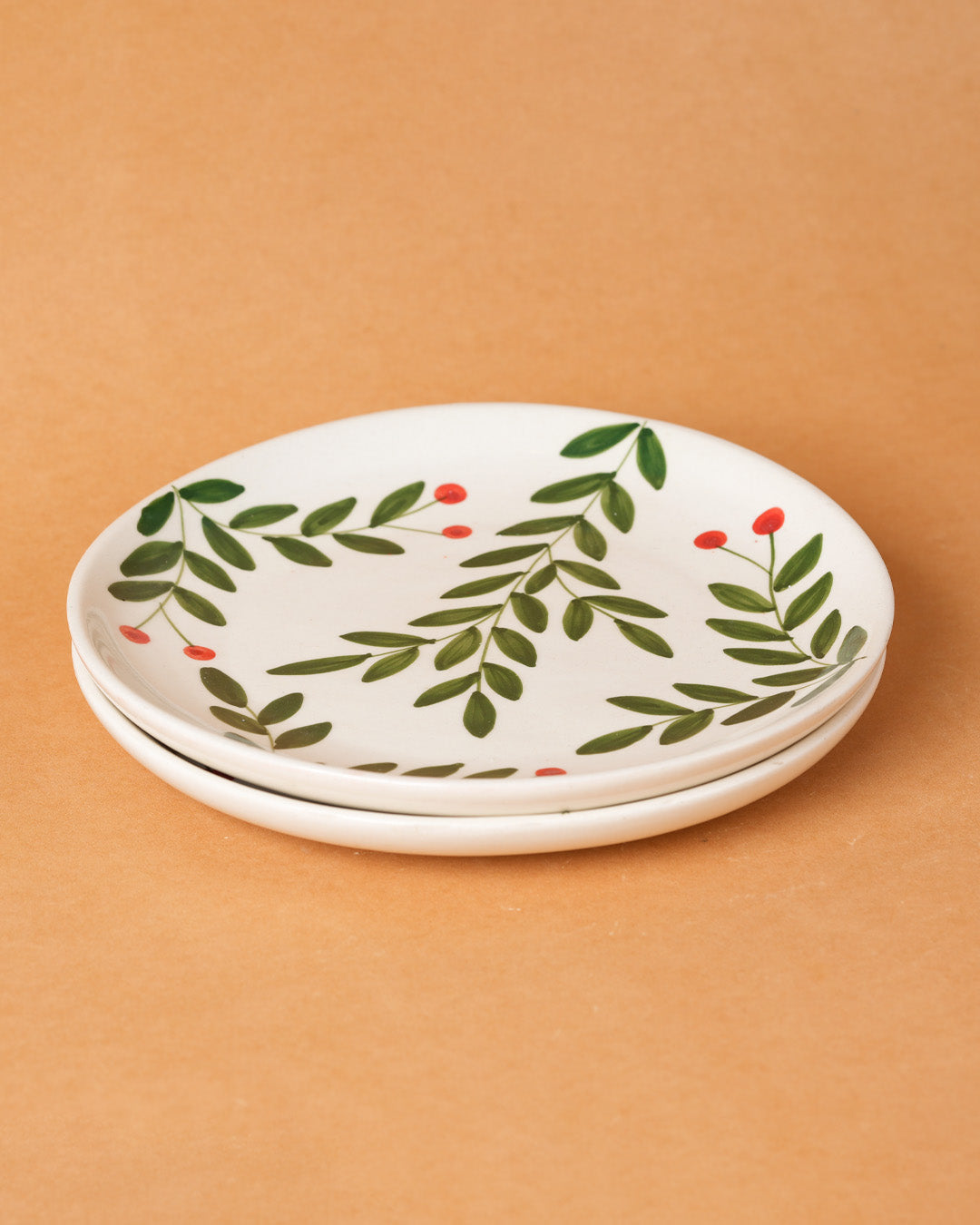 Set of two ceramic plates with leaf and berry design on a beige background