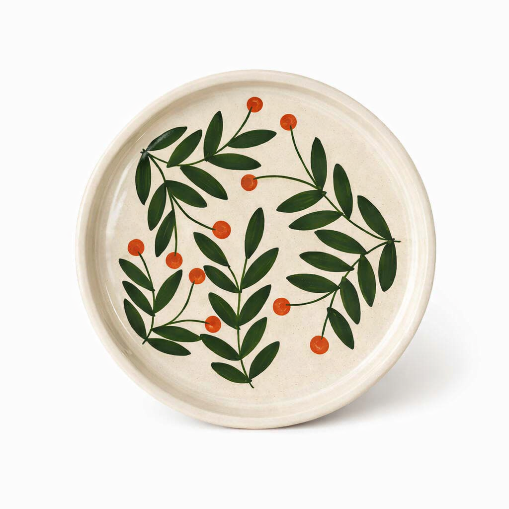Ceramic plate with green leaf and red berry design on a white background