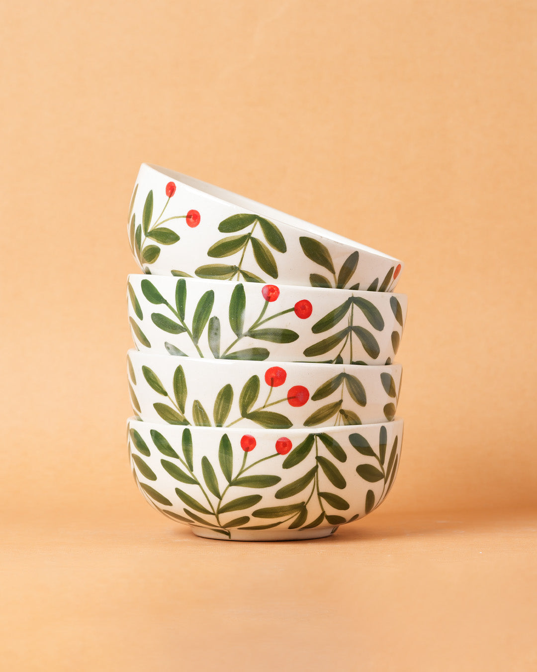 Stack of four ceramic bowls with leaf and berry pattern on a beige background