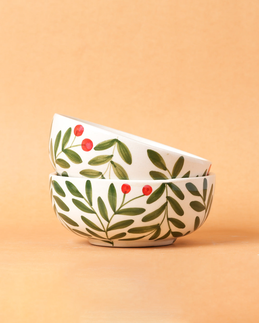 Two ceramic bowls with leaf and berry design on a beige background