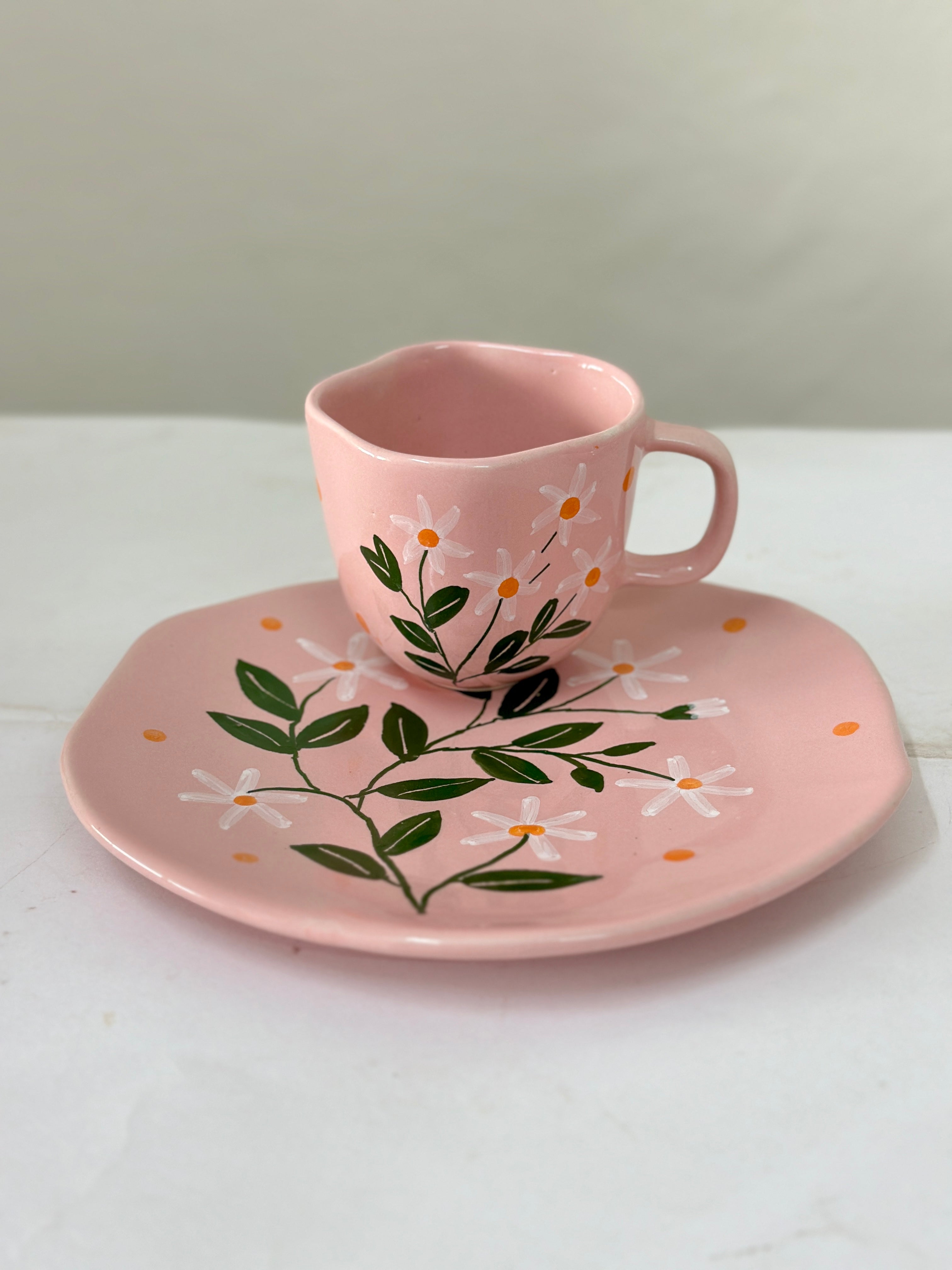 Pink ceramic cup and saucer with floral design on a white background