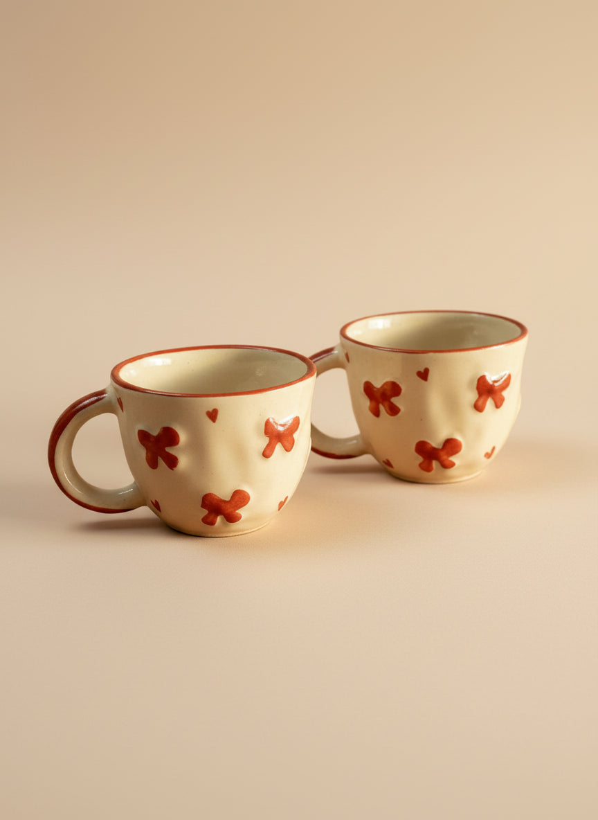 Two ceramic mugs with red butterfly designs on a beige background