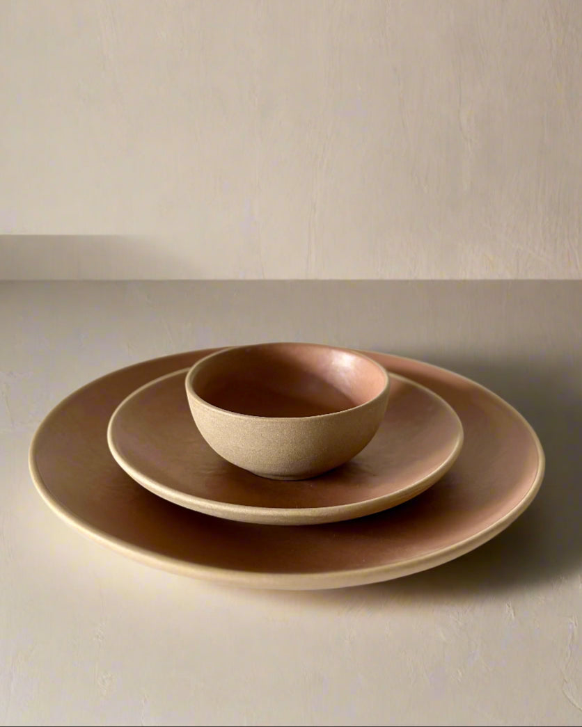 Set of ceramic bowls and plates in brown on a white surface with a light beige background