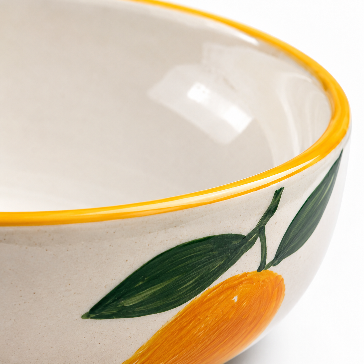 Ceramic bowl with yellow rim and orange and green leaf design on a white background
