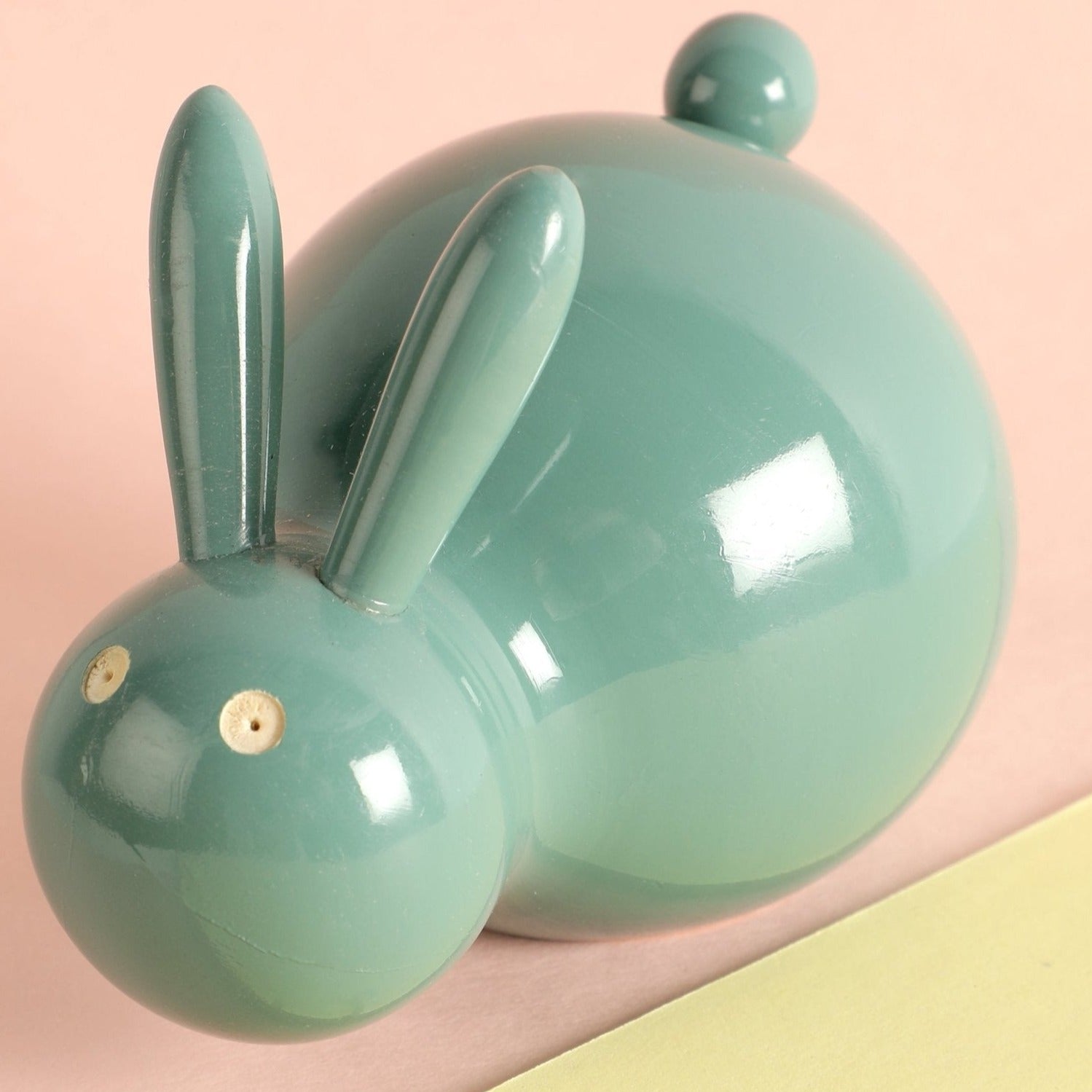 a green ceramic rabbit figurine sitting on a yellow and pink surface
